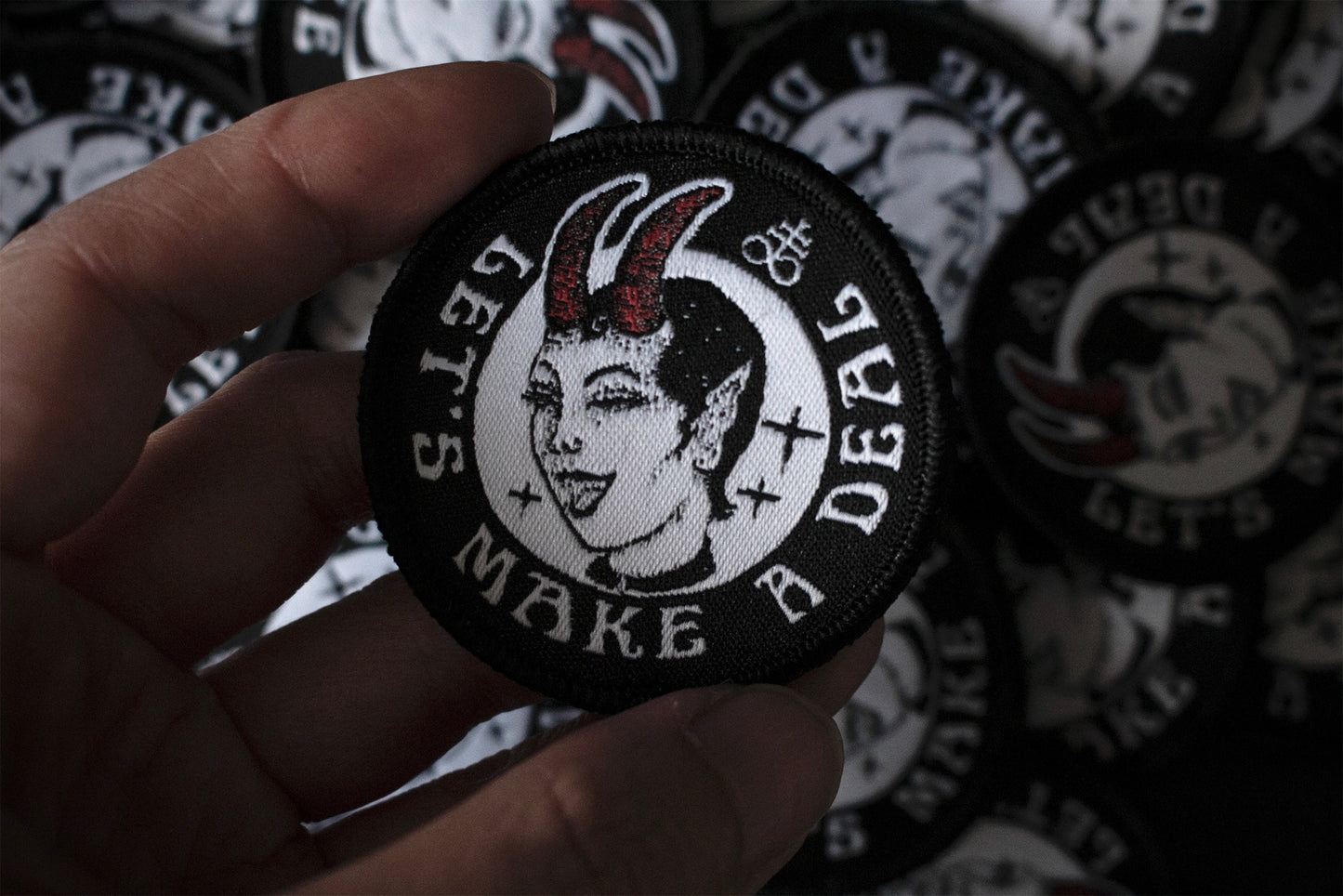 A round patch with the text let's make a deal, a devil woman winking, featuring a leviathan cross