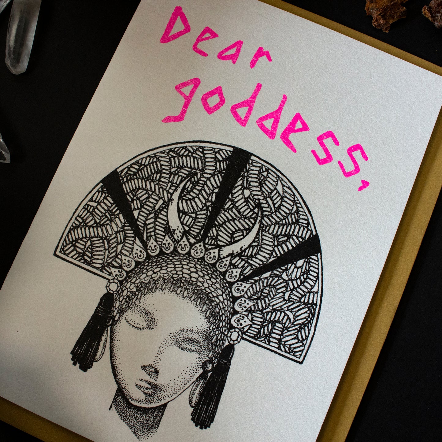 Dear Goddess greeting card and gold paper envelope on dark wood background.
